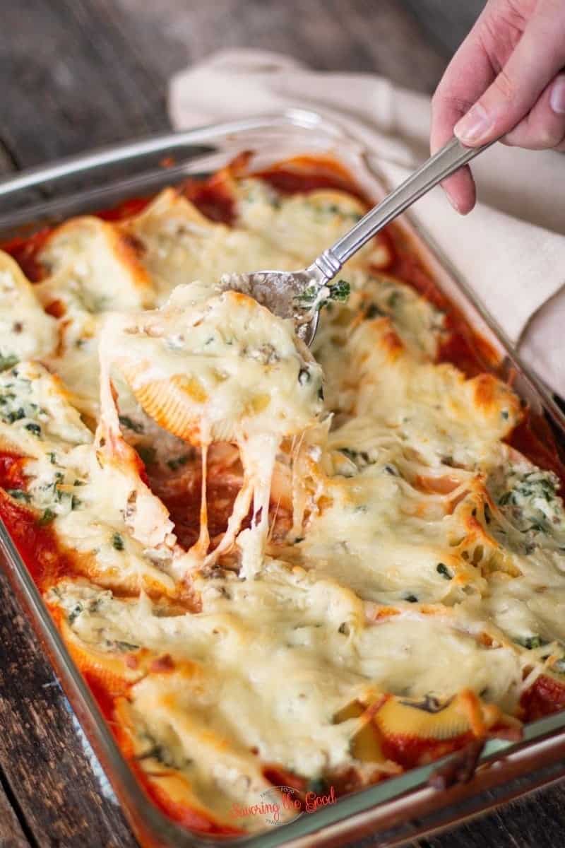a single stuffed shell being pulled from a full pan, the mozzarella cheese is pulling