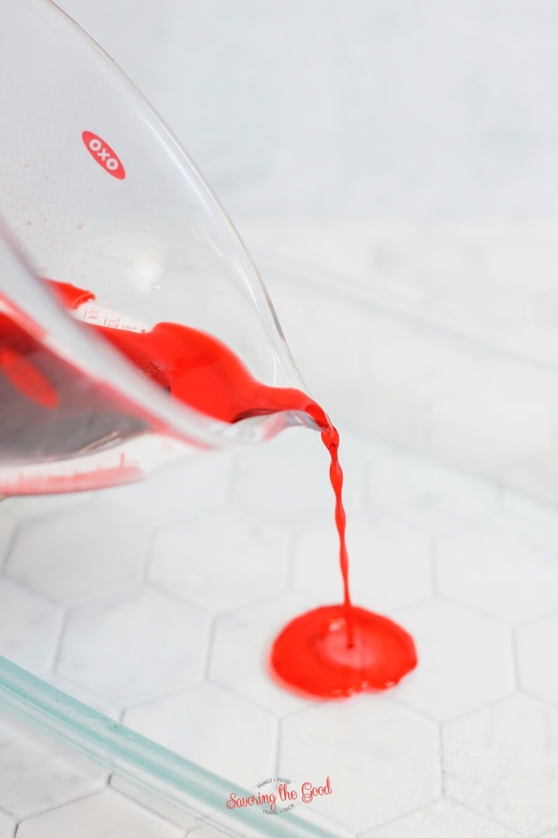 red jello being poured in a glass baking dish