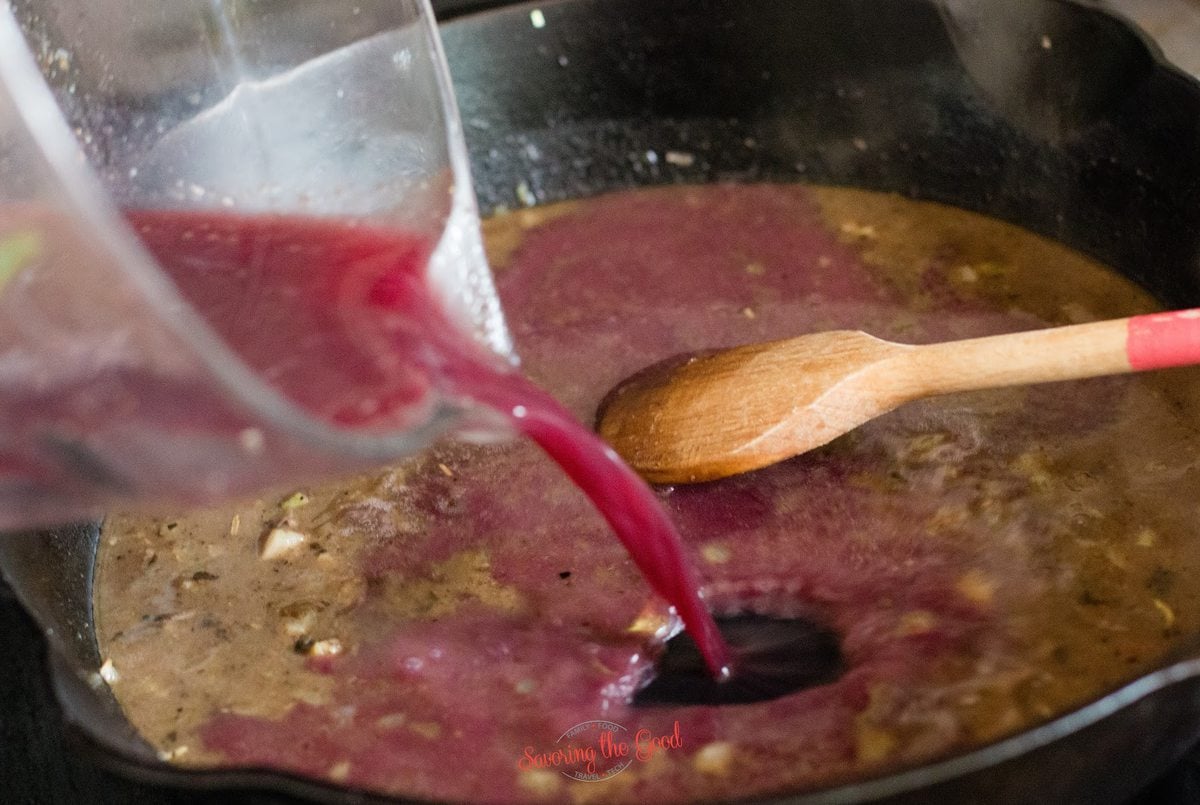 adding red wine to a hot pan to make red wine reduction and a wooden spoon