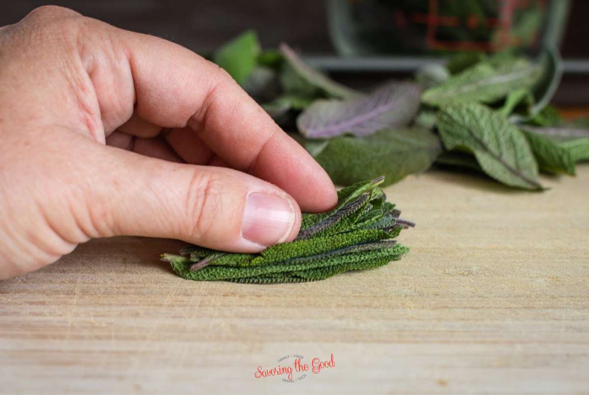 female hand stacking sage leaves for slicing on a wooden board