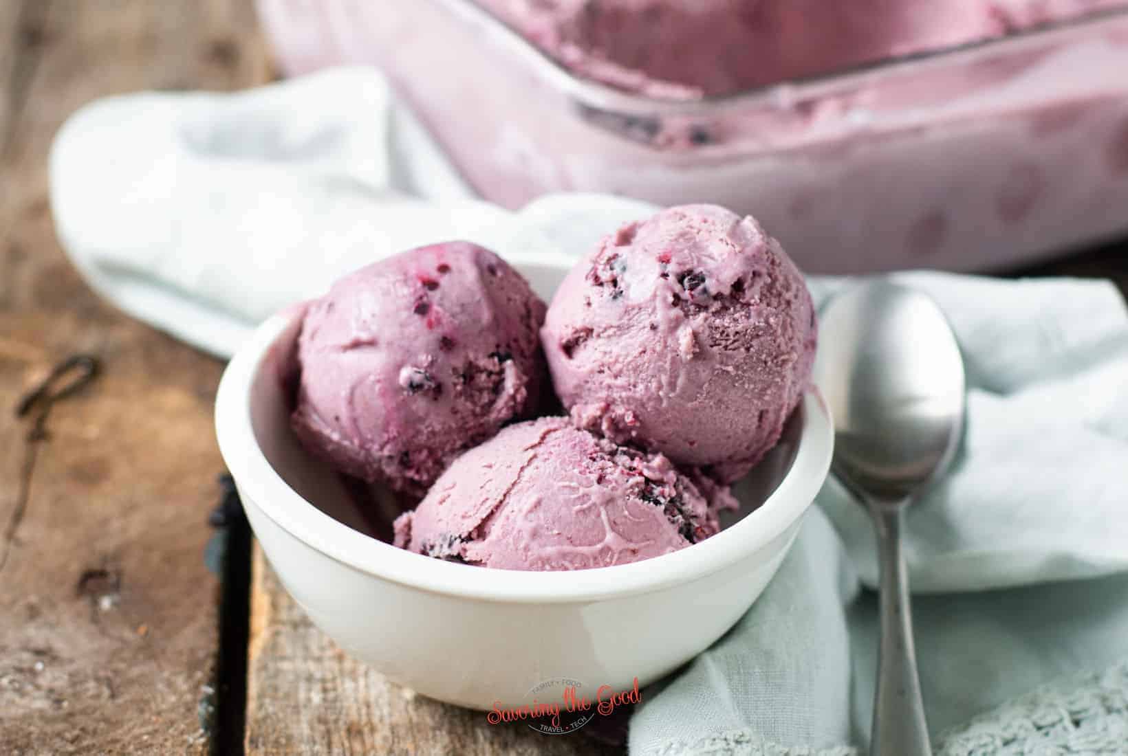 3 scoops of black raspberry ice cream in a white bowl with the container in the background