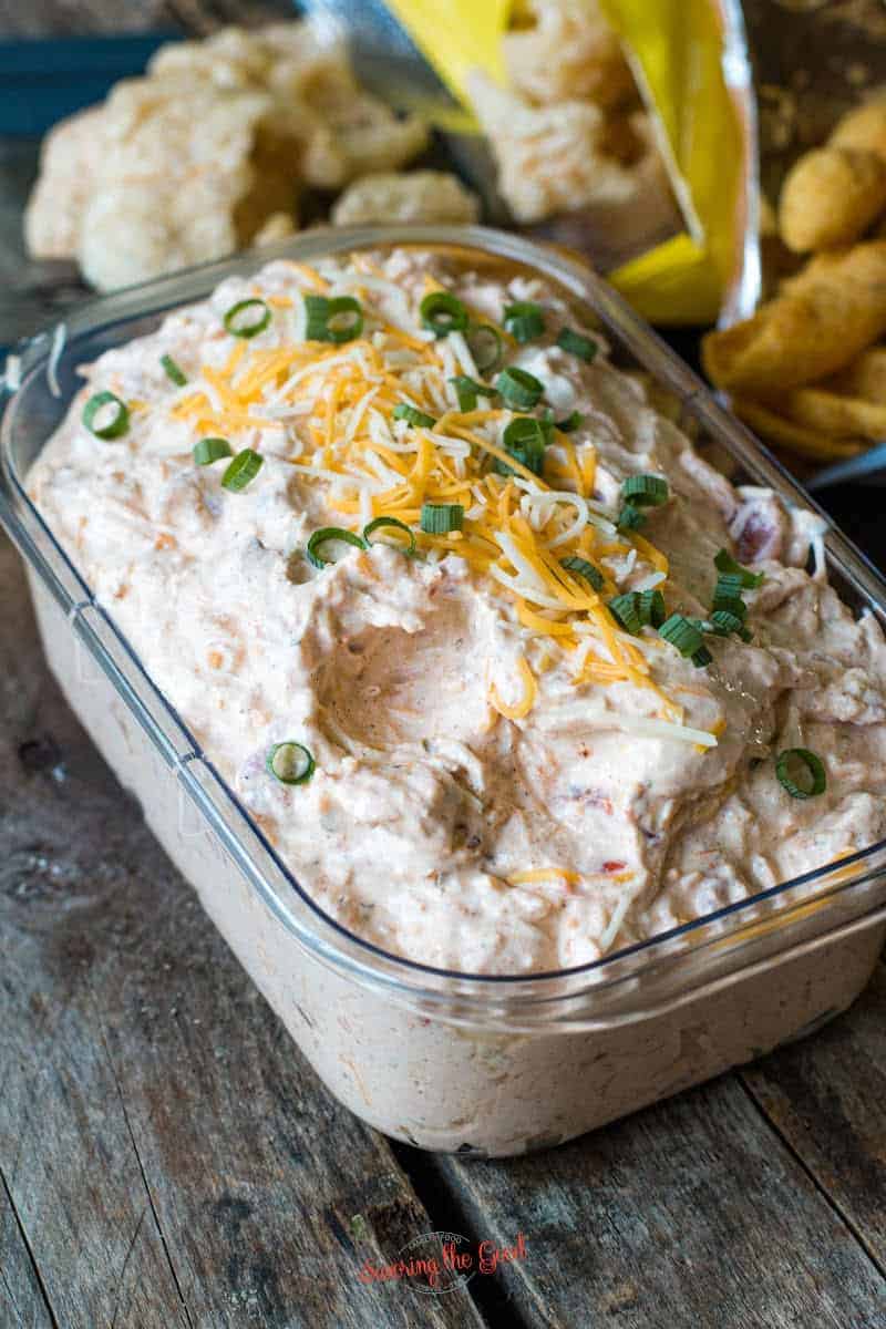 clear container full of dip with shredded cheese and chopped chive garnish