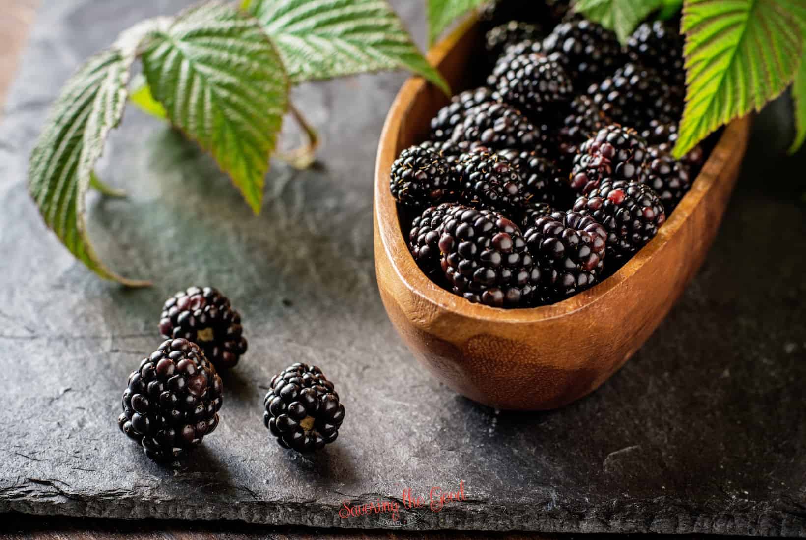 Blackberries in a wooden bowl on a slate table.