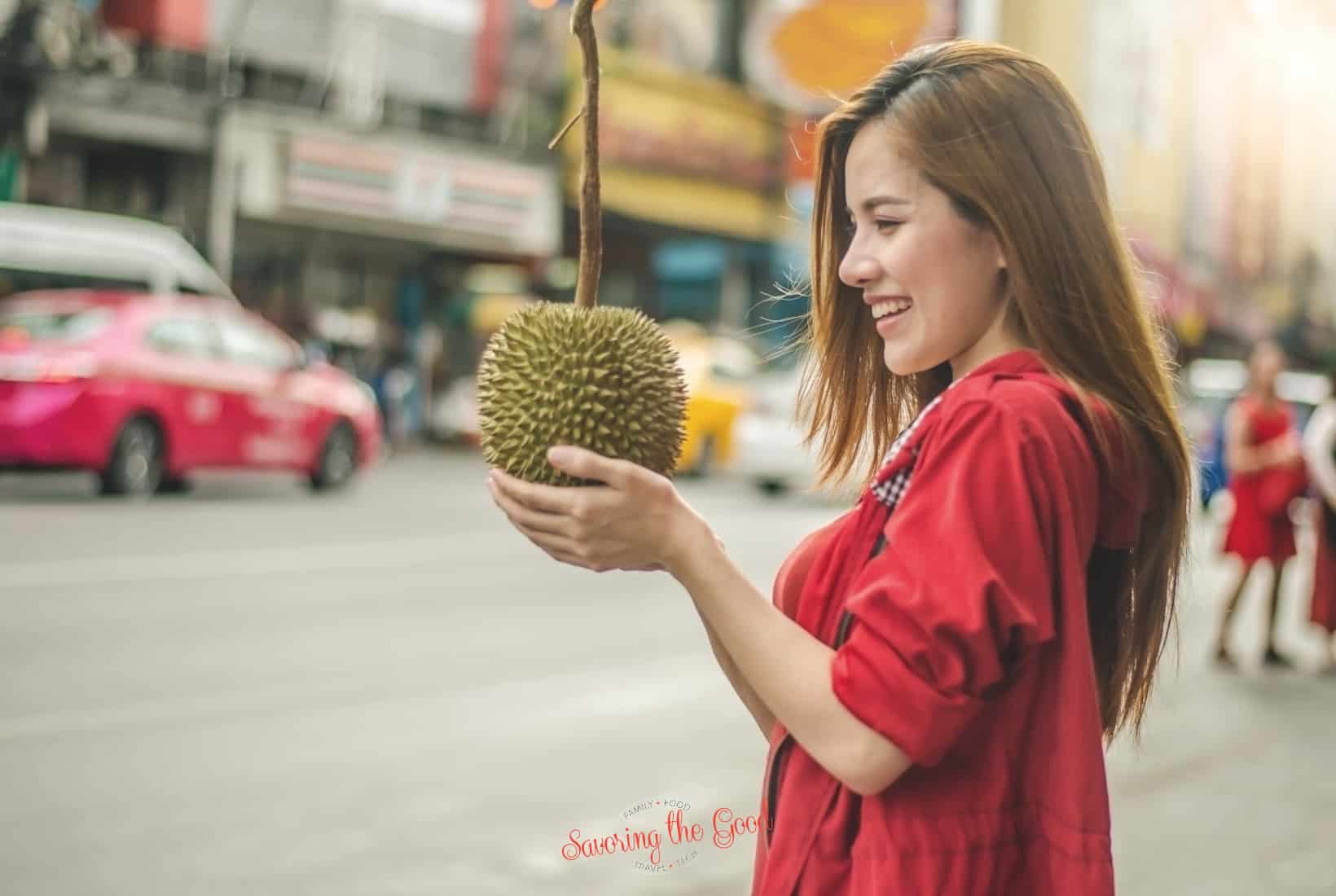 A woman holding a durian fruit on the street.