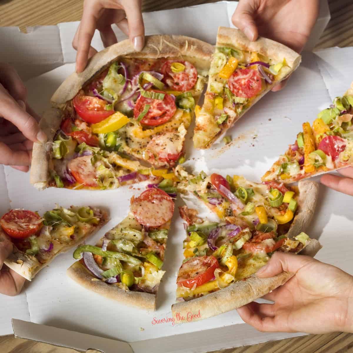 A group of people holding a pizza in a box. for featured image of what sides to serve with pizza.
