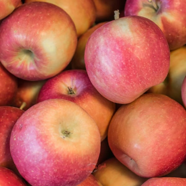 Many pink lady apples are piled up in a pile.