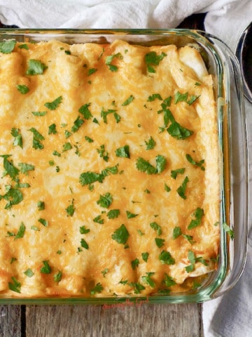 glass pan of Sour Cream Chicken Enchiladas with a serving spoon to the right side