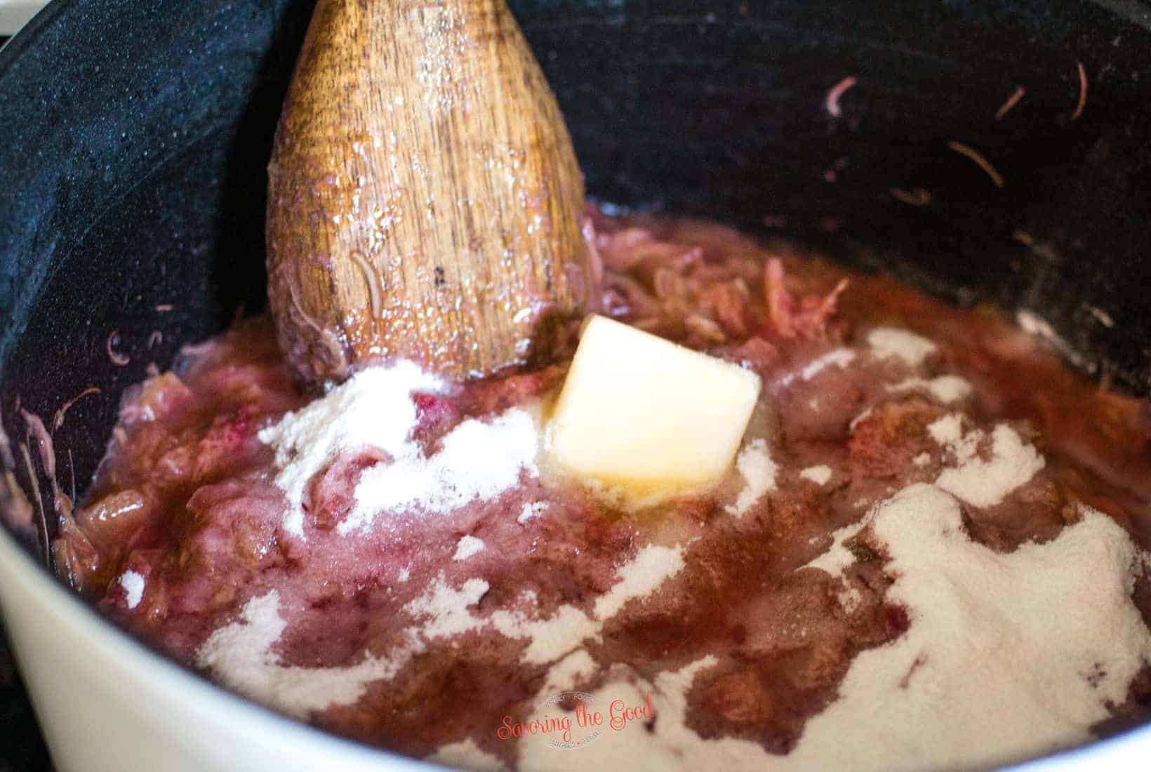 adding pectin and butter into the cooked rhubarb in a pot, wooden spoon stiring