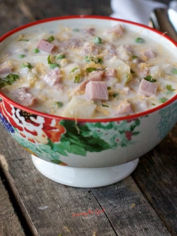 bowl of ham and potato soup with parsley garnish, sitting on a rustic wooden table, spoon and white napkin in the background