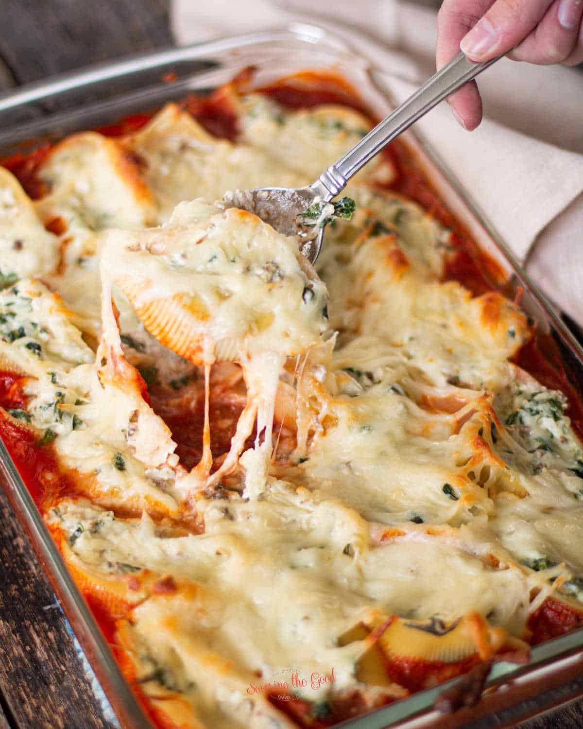 a single stuffed shell being pulled from a full pan, the mozzarella cheese is pulling 