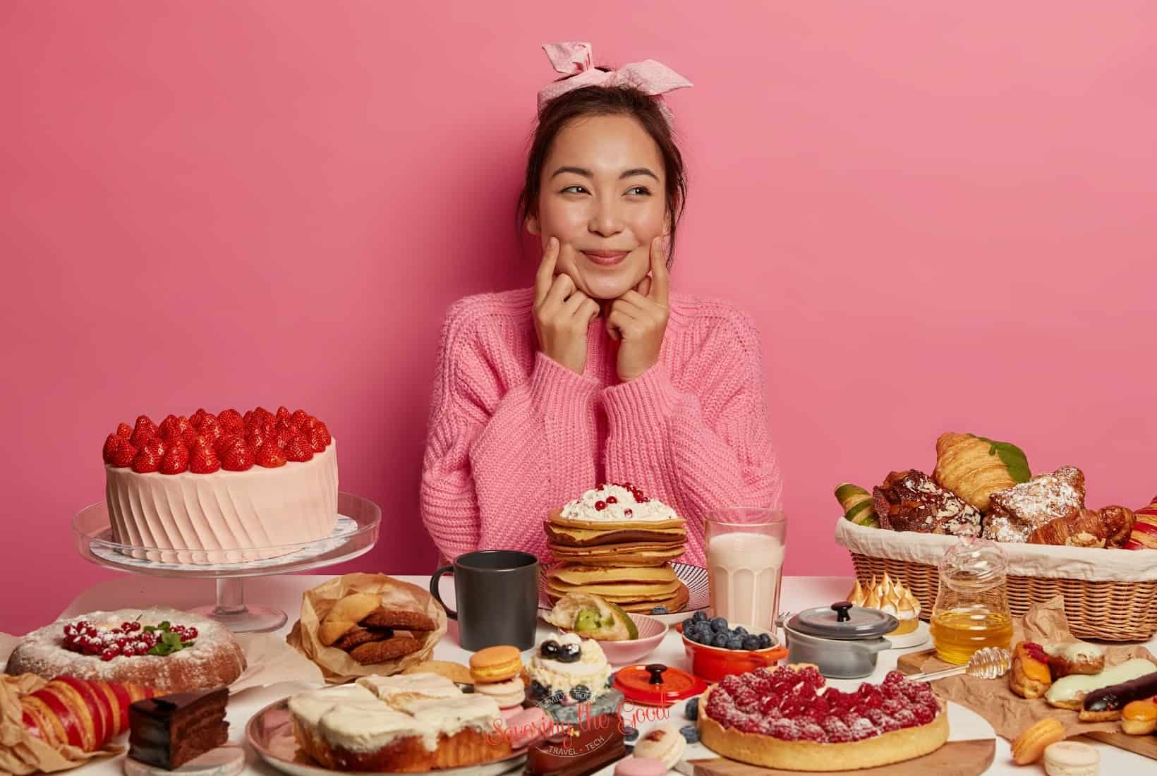 A young asian woman sitting at a table with a lot of desserts.