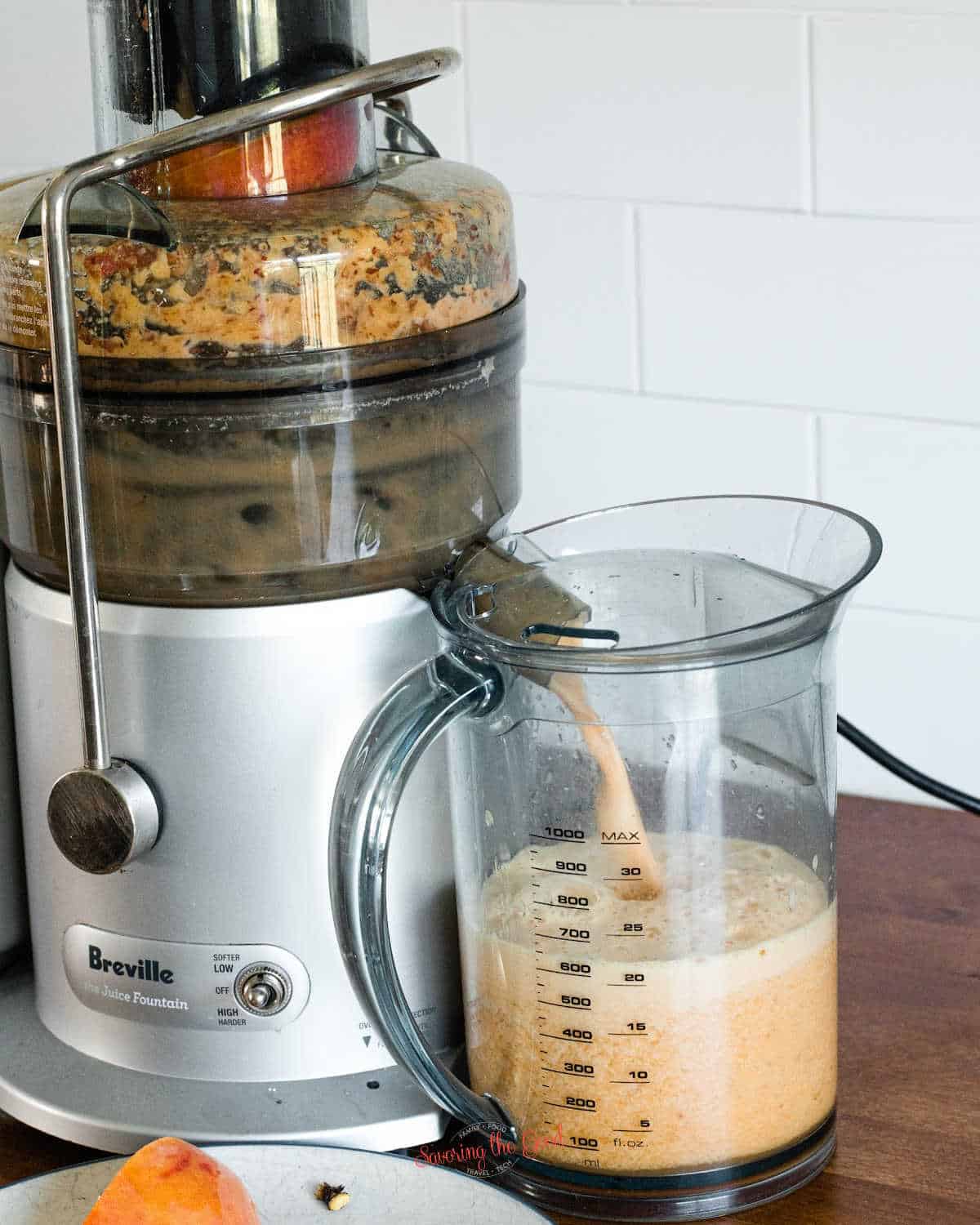 peaches being juiced in a breville fresh juice fountain, white tile backsplash in the background