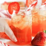 Two glasses of homemade strawberry tea with straws and fresh strawberries.