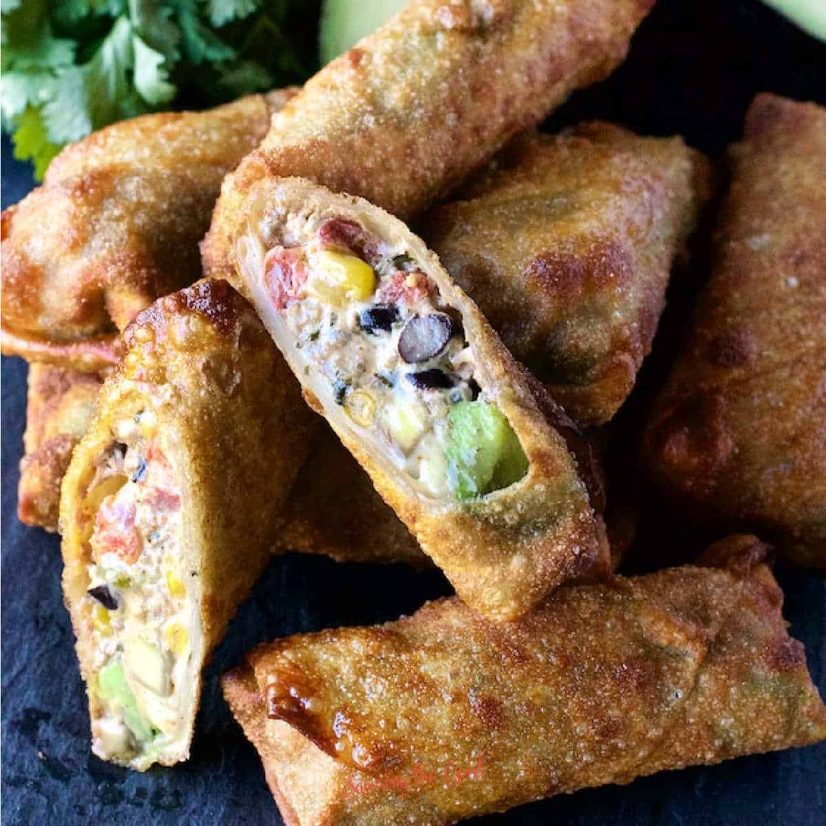 fried tex mex egg roll with beeg, cheese, corn, tomatoes, cream cheese black beans, cut open on the bias to show texture. Sitting on a pile of the rest of the the golden egg rolls