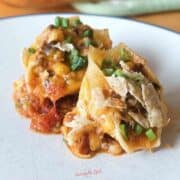2 taco stuffed shells on a white plate with crushed tortilla chips and sliced green onions for garnish