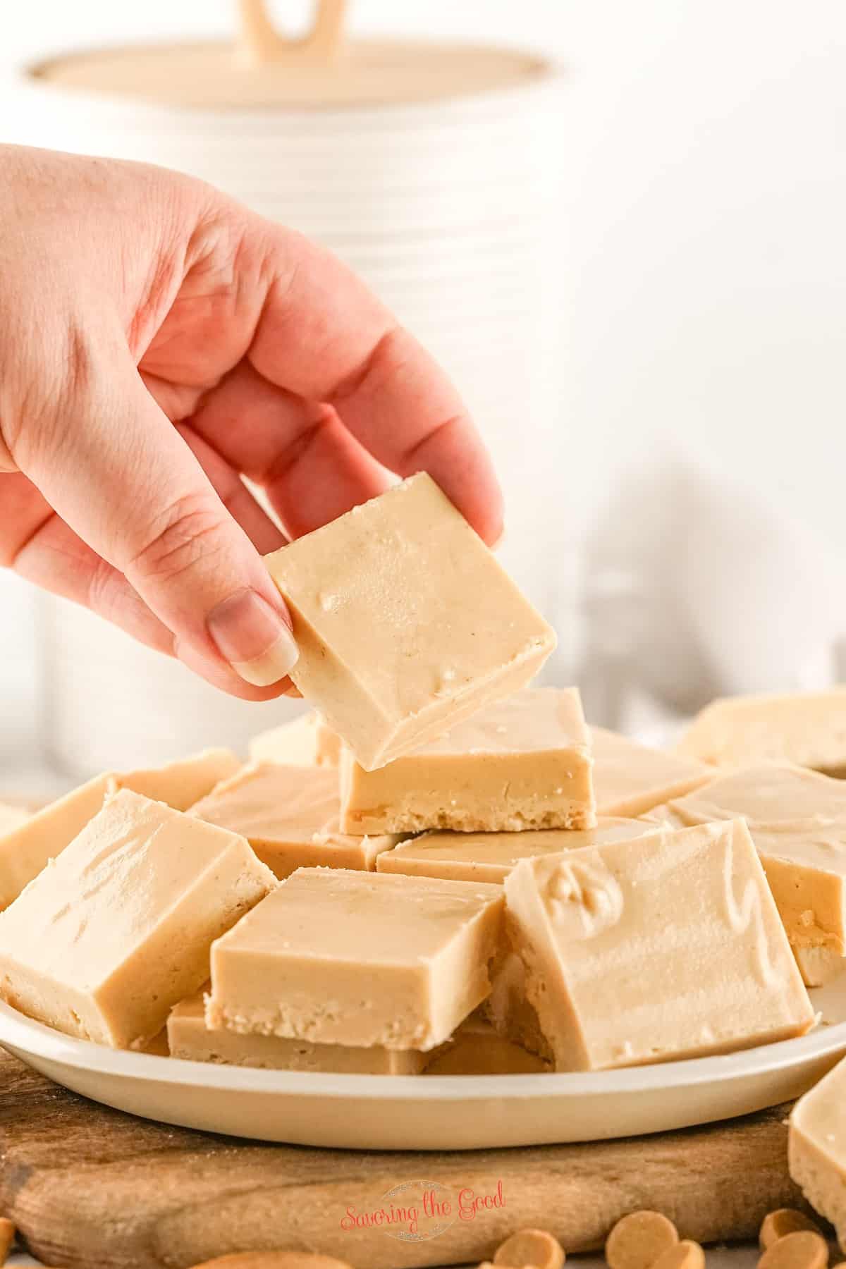 A hand grabbing pieces of peanut butter fudge on a plate. 2 ingredient peanut butter fudge recipe.