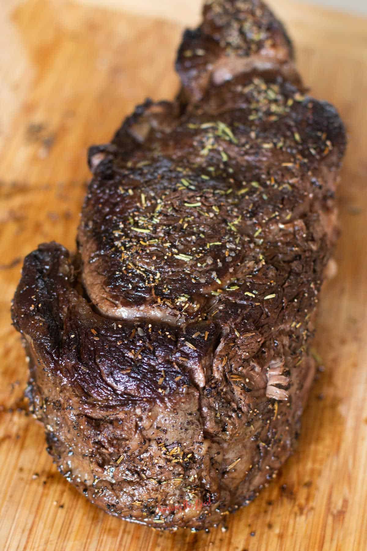 herb crusted prime rib resting on a bamboo cutting board vertical image
