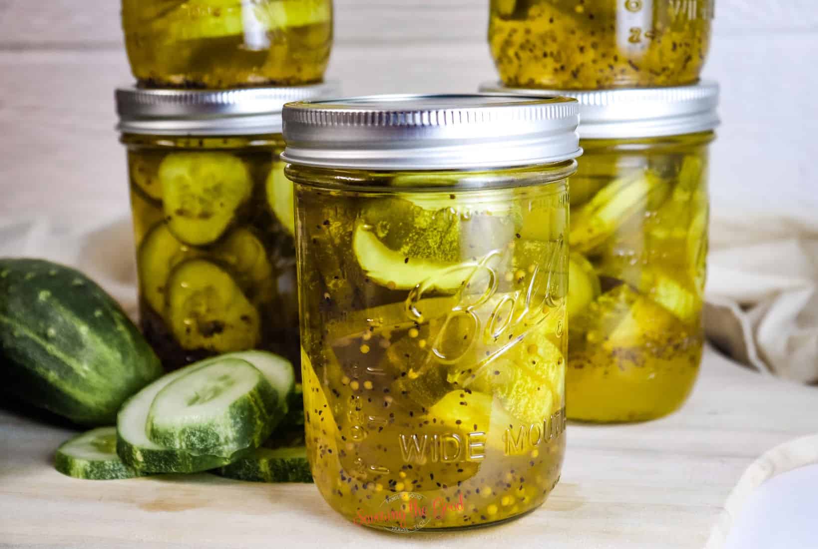 horizontal image of bread and butter pickles in 4 diggerent canning jars, with metal rings
