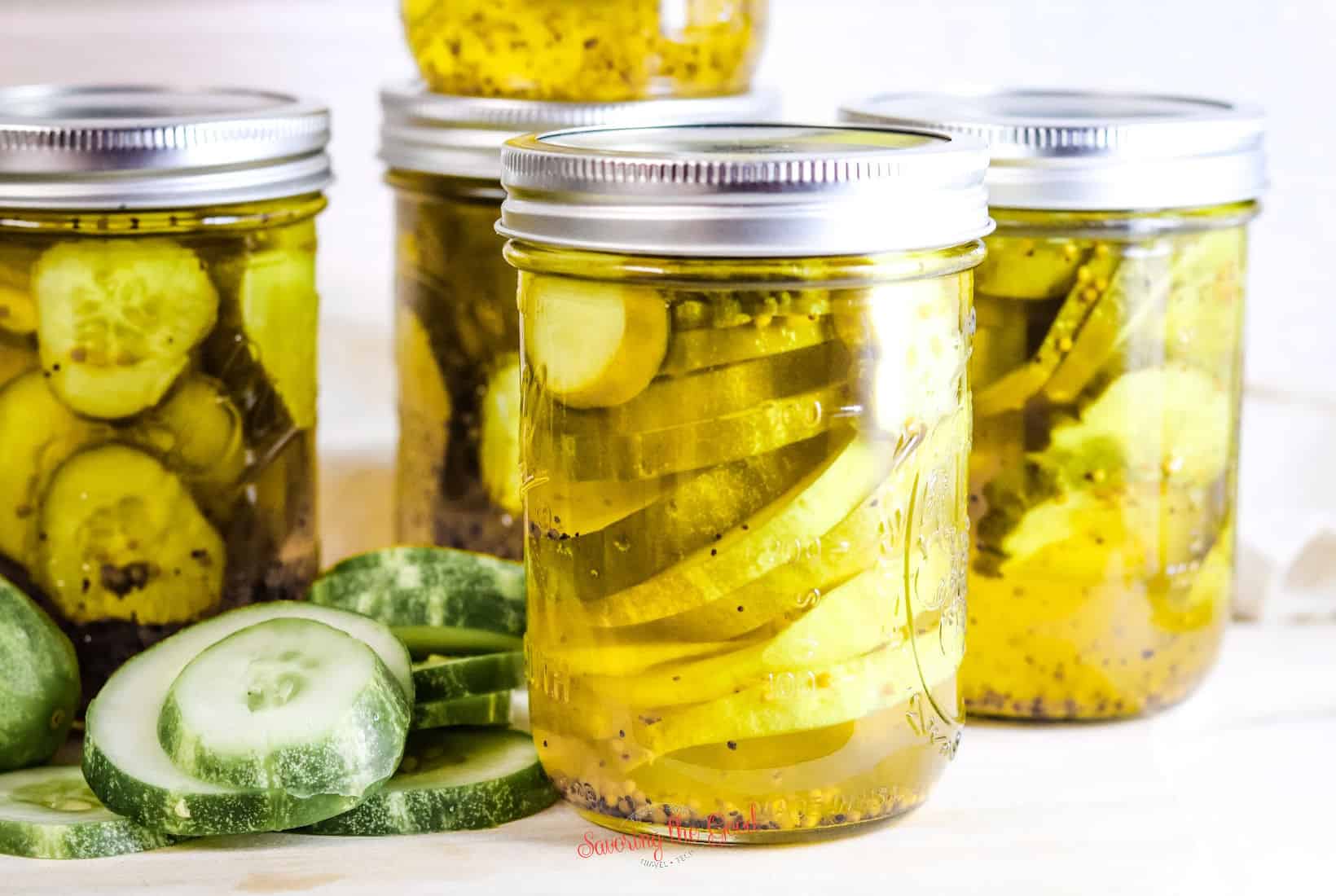 sliced cucumbers next to 3 jars of pickles