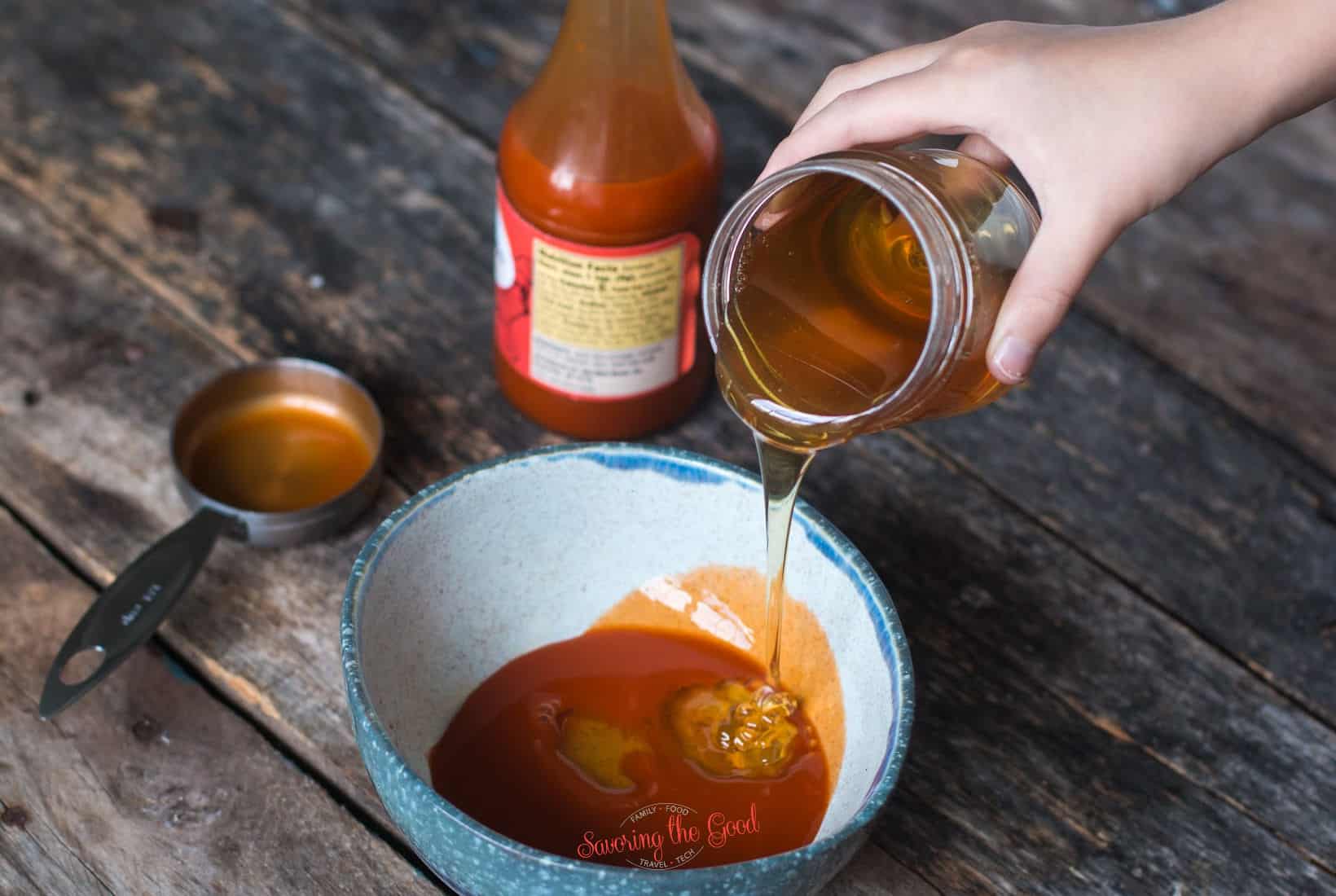 hand pouring honey into a bowl with hot sauce