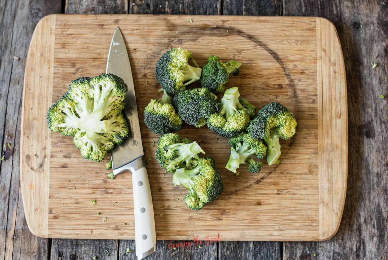 crown of broccoli with a chef knife, broccoli flourettes on the side