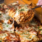lasagna roll up on a serving fork coming out of the full pan, cheese pulling
