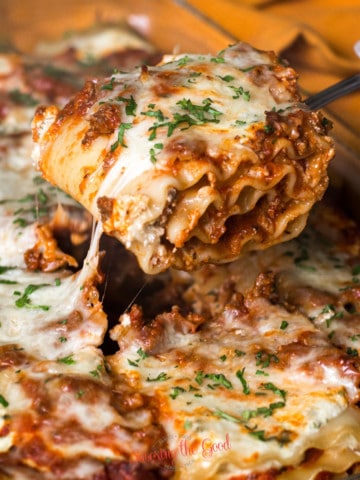 lasagna roll up on a serving fork coming out of the full pan, cheese pulling