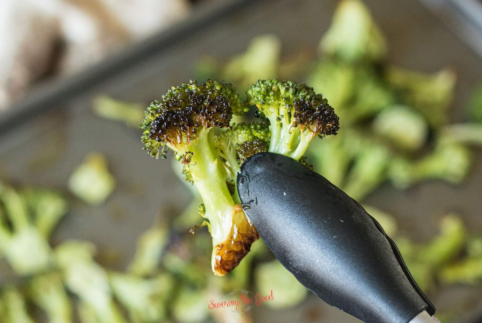 tongs holding a piece of pan roasted broccoli