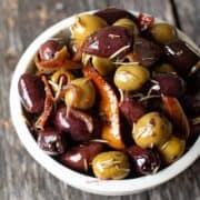 warm olive appetizer in a white bowl with orange peel and rosemary