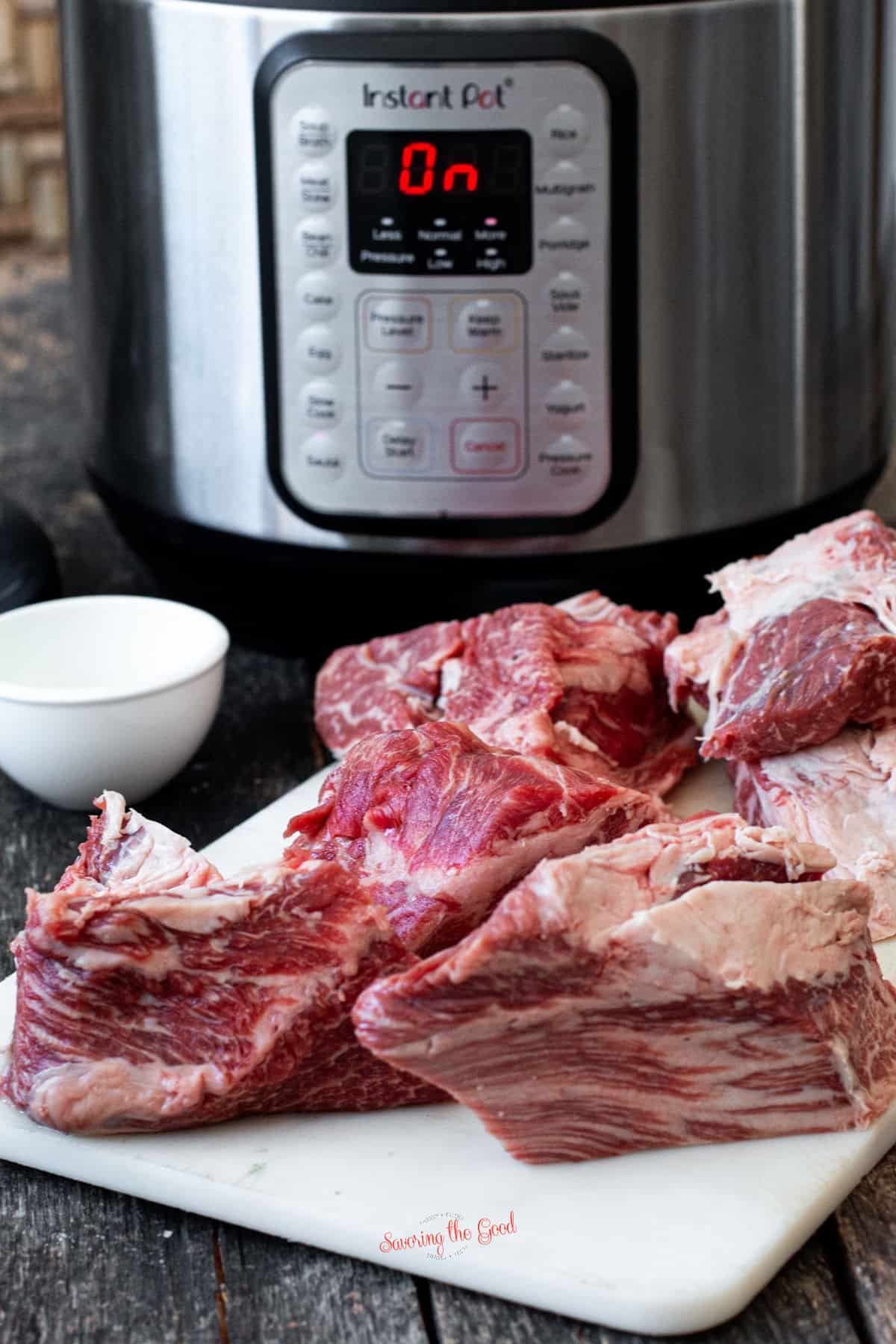 chuck roast chunks on a cutting board next to an instant pot