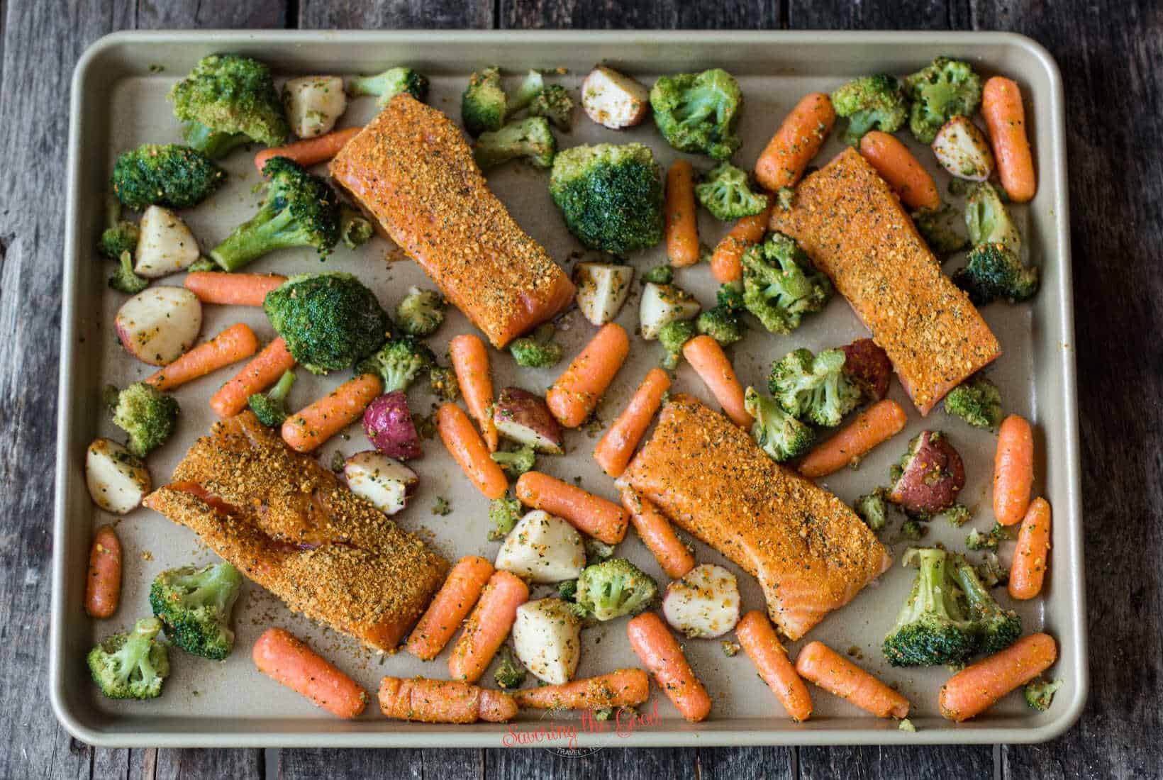 raw salmon and seasoned rw vegetables on a sheet pan for cooking.