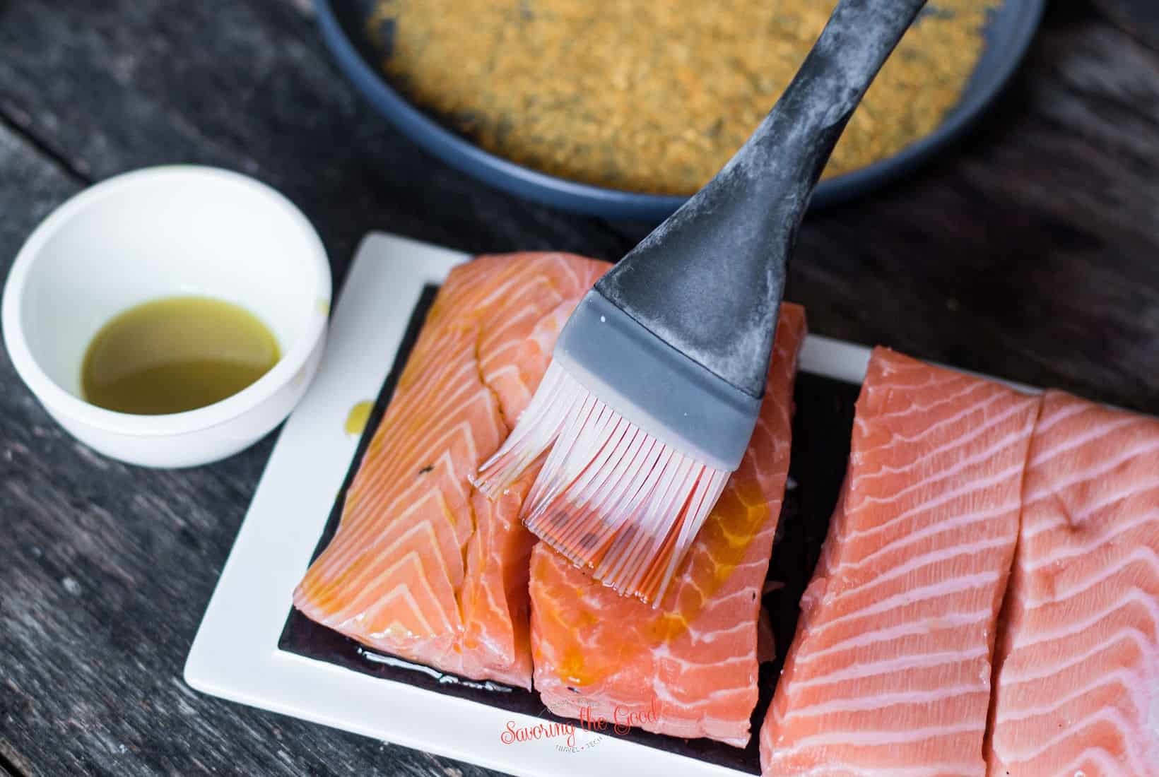 silicone pastry brush applying olive oil to the raw salmon filets.