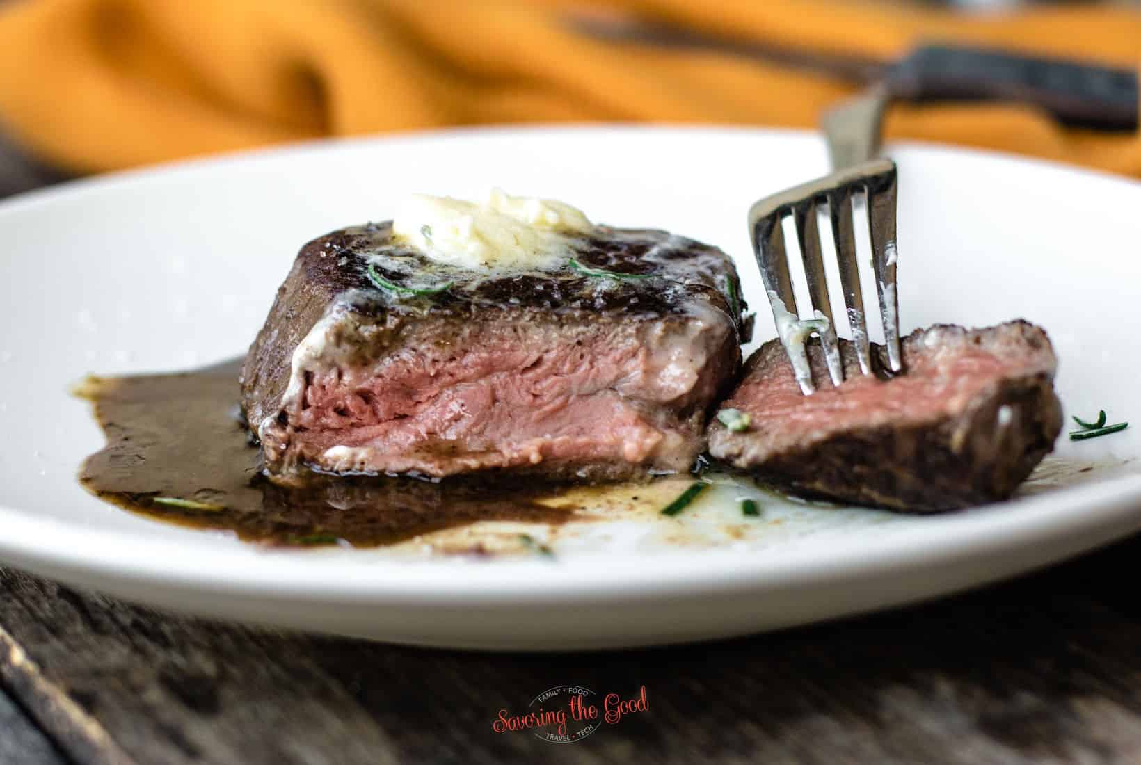 horizontal image of a sous vide filet mignon with a pat of butter, white plate, fork and orange napkin to the side.
