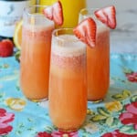 3 strawberry mimosas in stemless flutes with ½ strawberry garnish.
