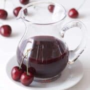 A pitcher of cherry juice, perfect for making a delicious cherry syrup recipe, placed on a white plate.