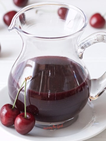 A pitcher of cherry juice, perfect for making a delicious cherry syrup recipe, placed on a white plate.