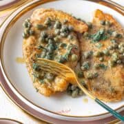 Chicken Piccata {Giada Recipe} on a plate with a gold colored fork cutting a cutlet.