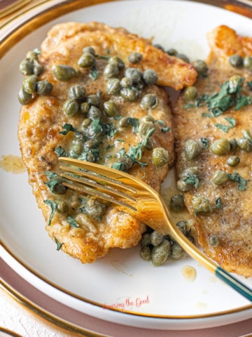 Chicken Piccata {Giada Recipe} on a plate with a gold colored fork cutting a cutlet.