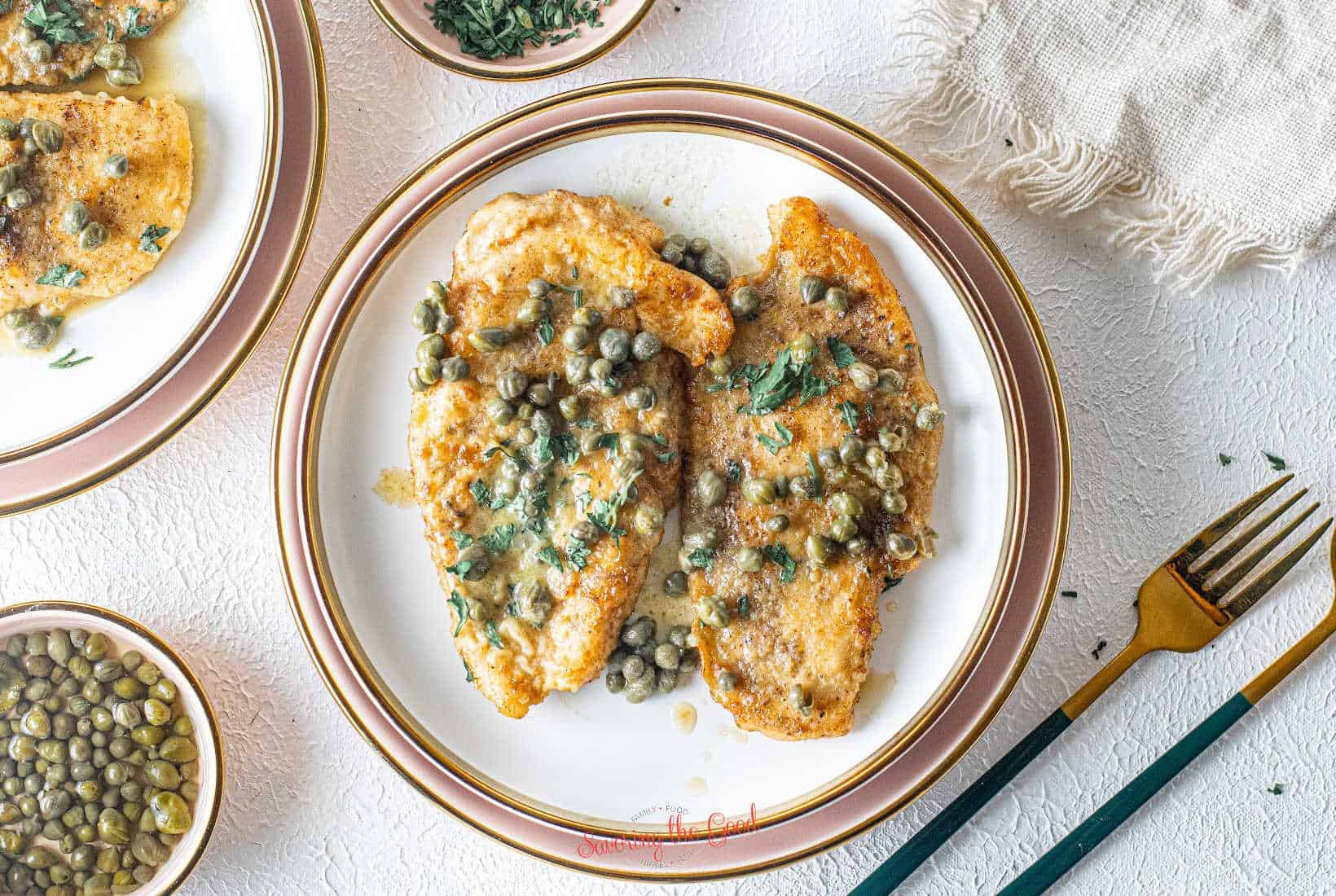Chicken Piccata {Giada Recipe} on a white plate with a light pink charger under the plate.