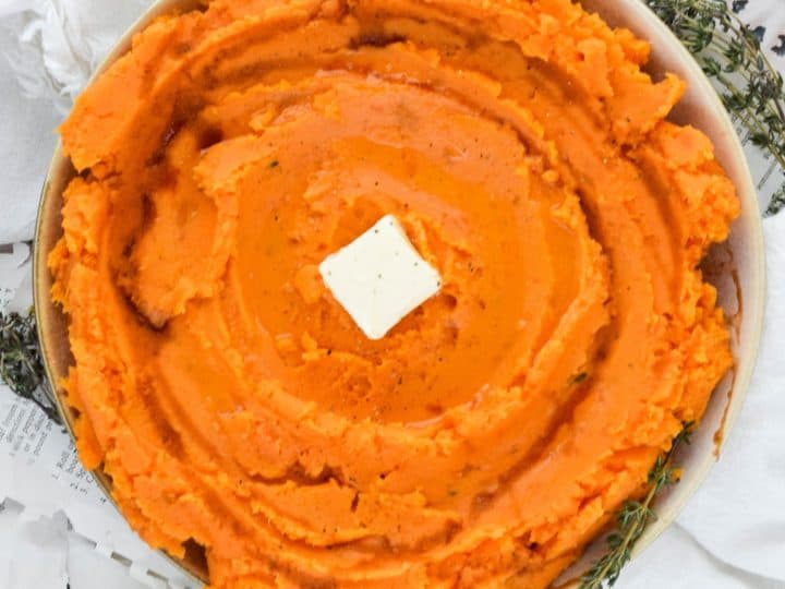 A bowl of sweet potato mashed potatoes with butter and sprigs of thyme.
