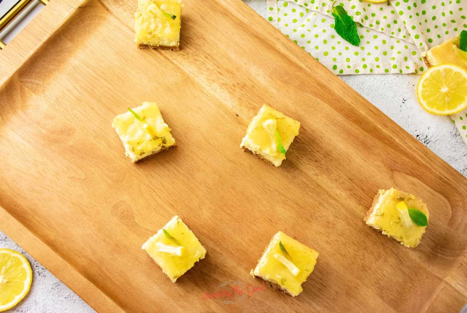 Lemon Cheesecake Bars with mint leaf garnish on a wooden serving board