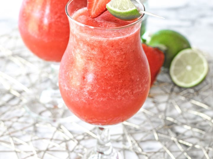 Strawberry Daiquiri in a hurricane glass with strawberry and lime garnish.