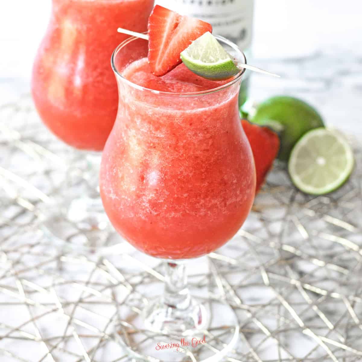 Strawberry Daiquiri in a hurricane glass with strawberry and lime garnish.