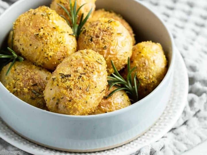 Roasted potatoes in a bowl with rosemary sprigs.
