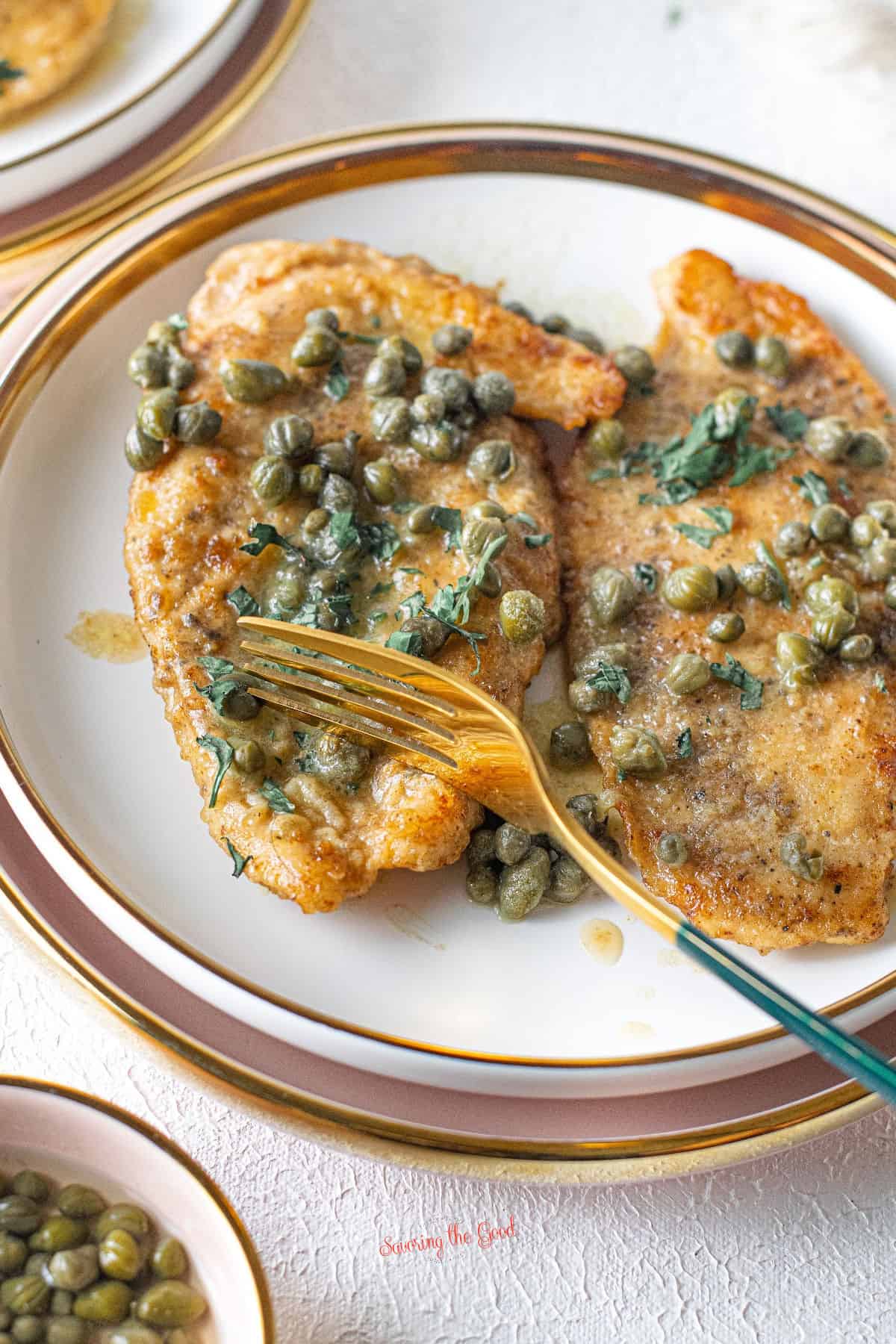 giada' chicken piccata on a plate with capers and parsley garnish.