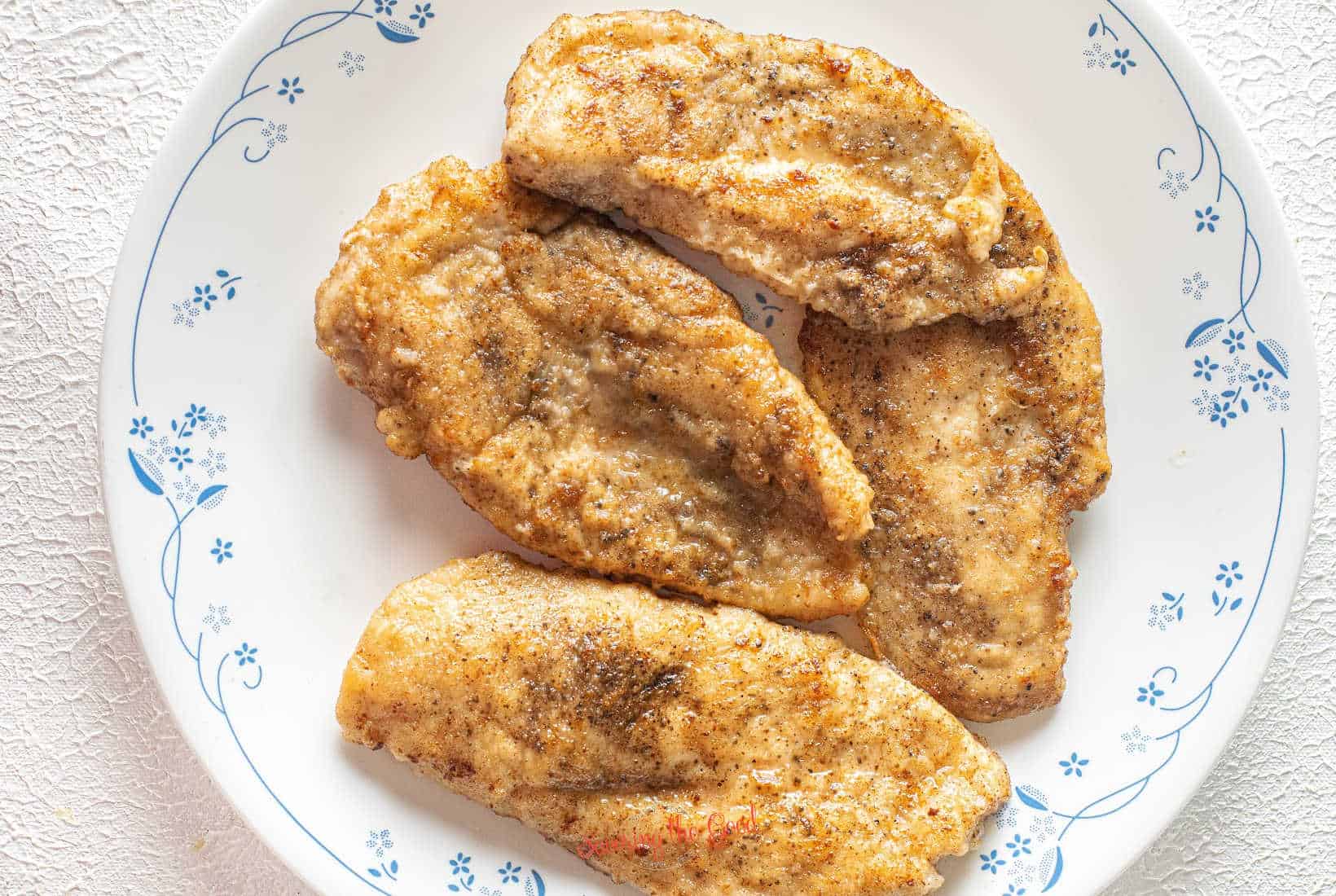 seared, dredged chicken cutlets on a white plate with delicate blue flowers on the plate.
