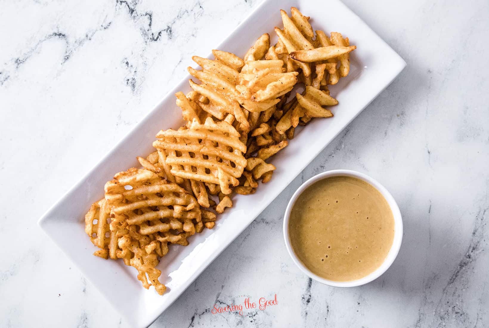 tray of crisp waffle fries on a white rectangle serving tray with chick fil a sauce in a white ramekin to the side.