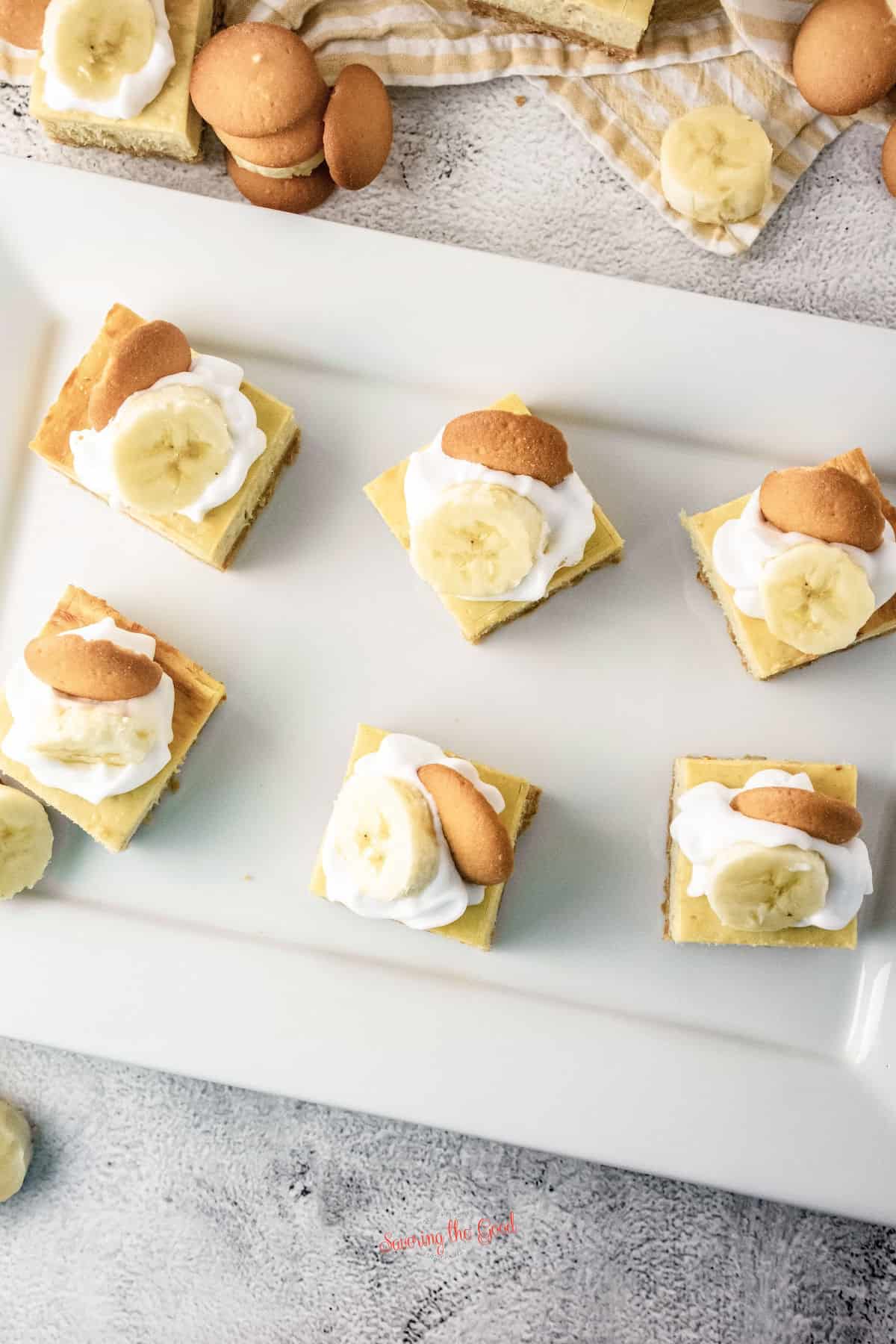 6 banana pudding cheesecake bars on a white rectangle servint tray, top down image.