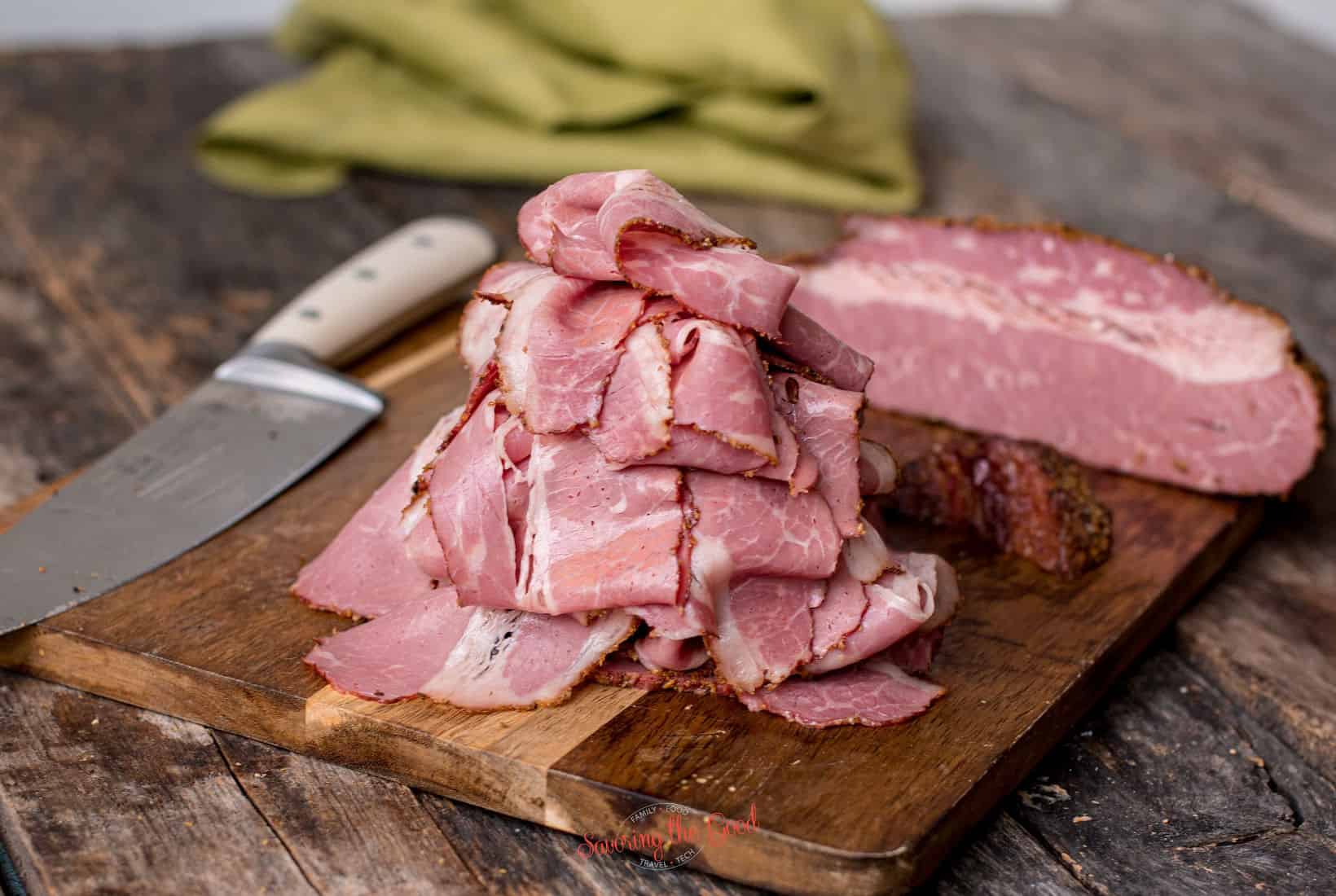 pile of sliced smoked corned beef on a cutting board with a knife to the side.