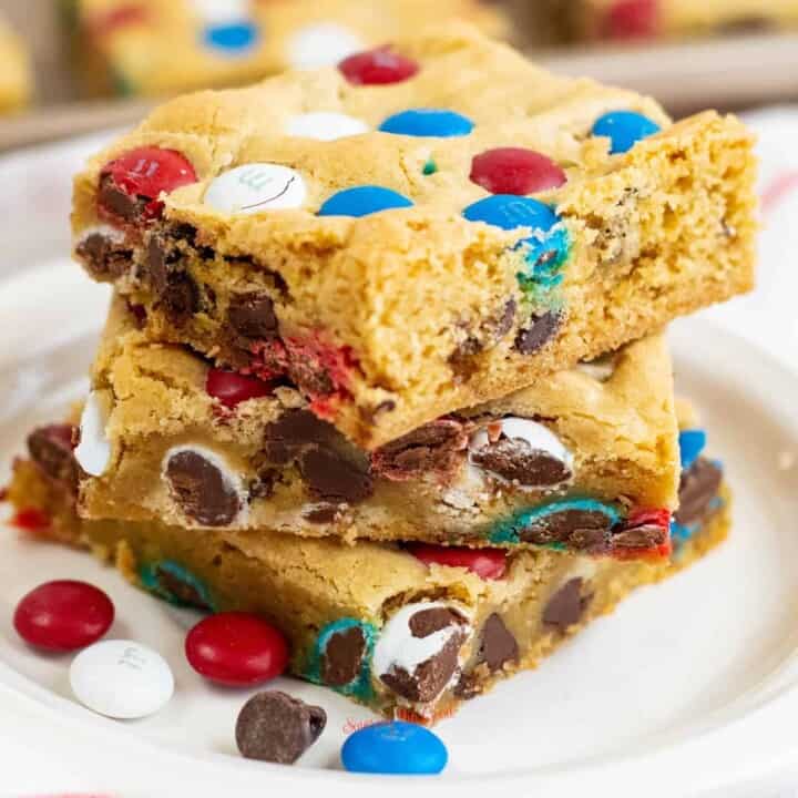 M&M cookie bars stacked on eachother on a white plate, square image.
